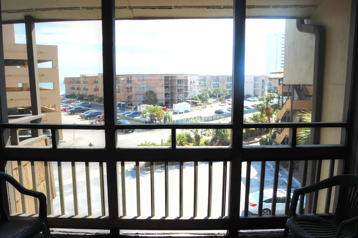 A relaxed balcony view overlooking the parking lot, neighboring buildings, and swaying palm trees. The atmosphere evokes unwinding outdoors, appreciating the mild winter climate, and enjoying Myrtle Beach’s coastal scenery from the comfort of your condo.